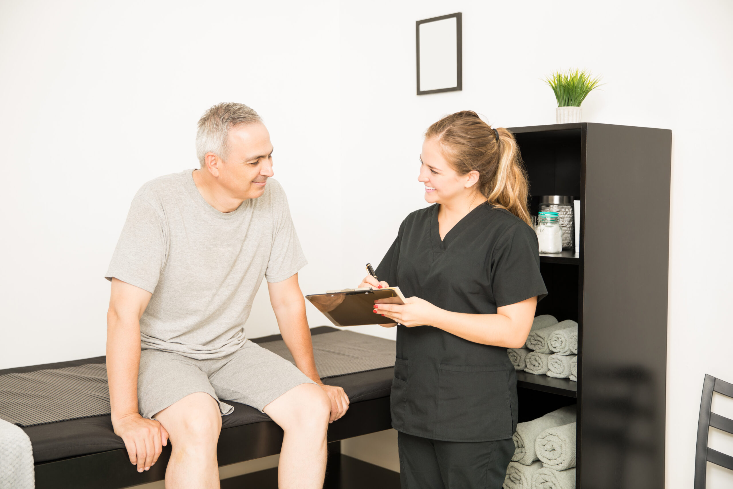 physiotherapist writing on clipboard while talking to elderly patient